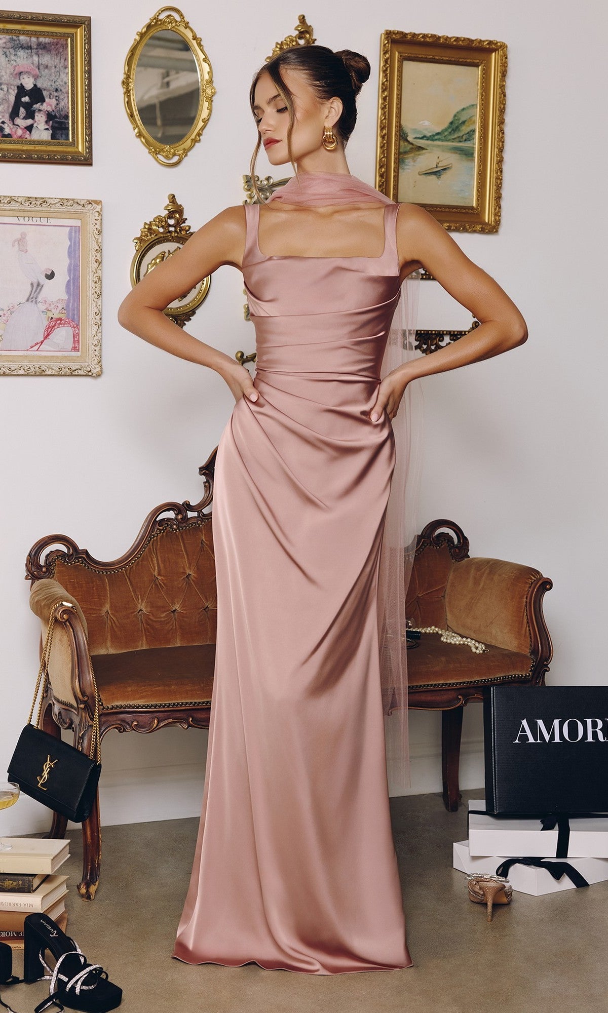 Woman in a taupe Long Prom Dress: Amoris T729 with a square neckline stands before a vintage sofa, surrounded by framed art, handbags, and gift boxes in a stylish room.